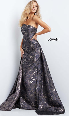 A woman poses with one hand on her hip against a plain background, wearing the Jovani 06255 Long Formal Dress—a strapless gown featuring a metallic, patterned finish. The word “JOVANI” appears beside her, spotlighting this stunning designer piece.