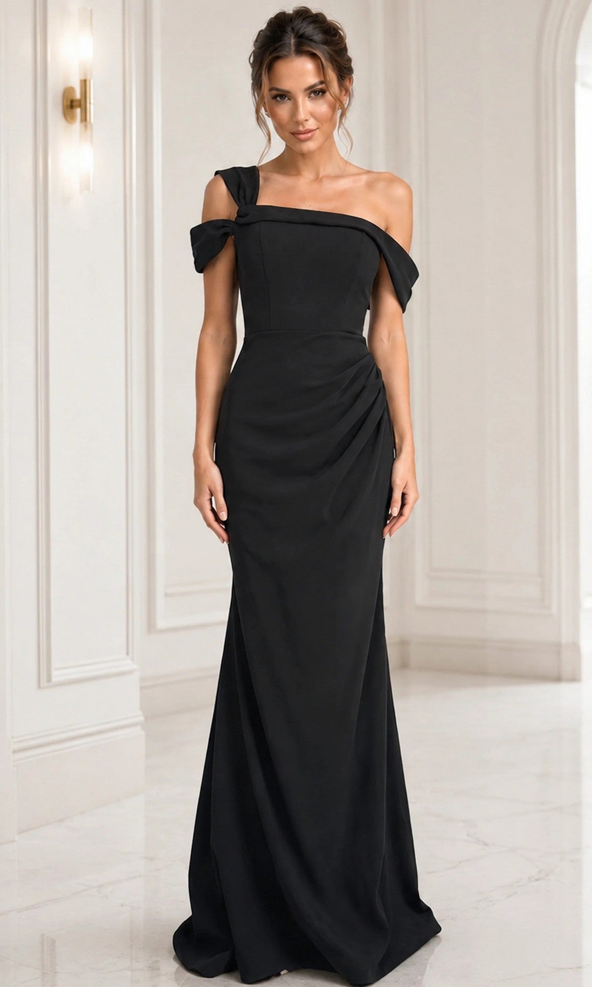 A woman is wearing the Long Formal Dress: Jovani 06723 in black—a floor-length, off-shoulder gown with a sheath silhouette—as she stands indoors on a marble floor with light-colored walls in the background.