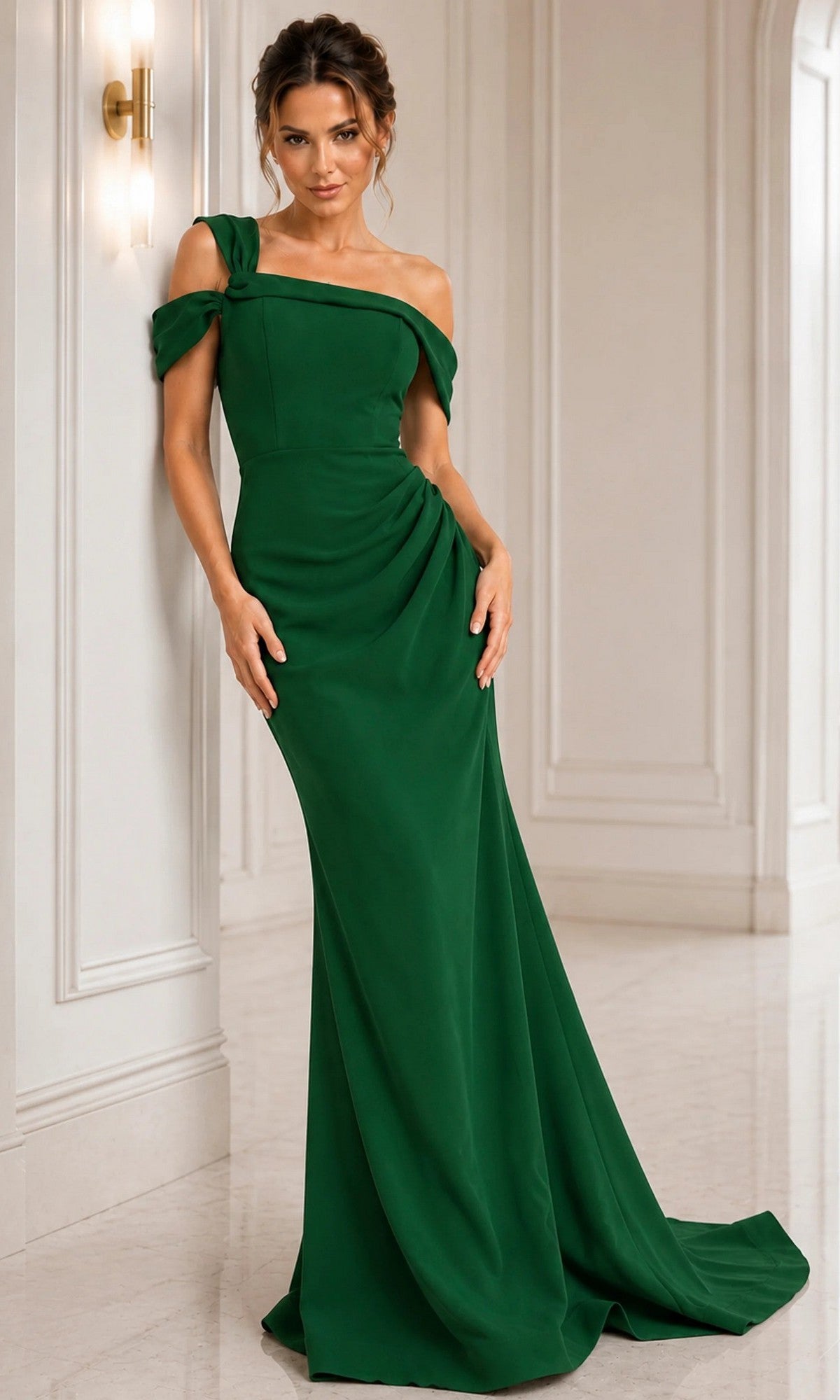 Dressed in the elegant Jovani 06723 long formal dress in emerald, a woman stands against a white, paneled wall with a wall sconce—the off-the-shoulder sheath silhouette evokes timeless classic style.
