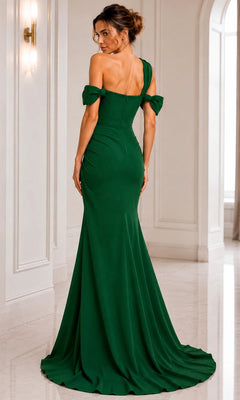 A woman stands in a white, elegant hallway wearing the Long Formal Dress: Jovani 06723—a fitted, floor-length green gown with off-the-shoulder sleeves and a slight train.