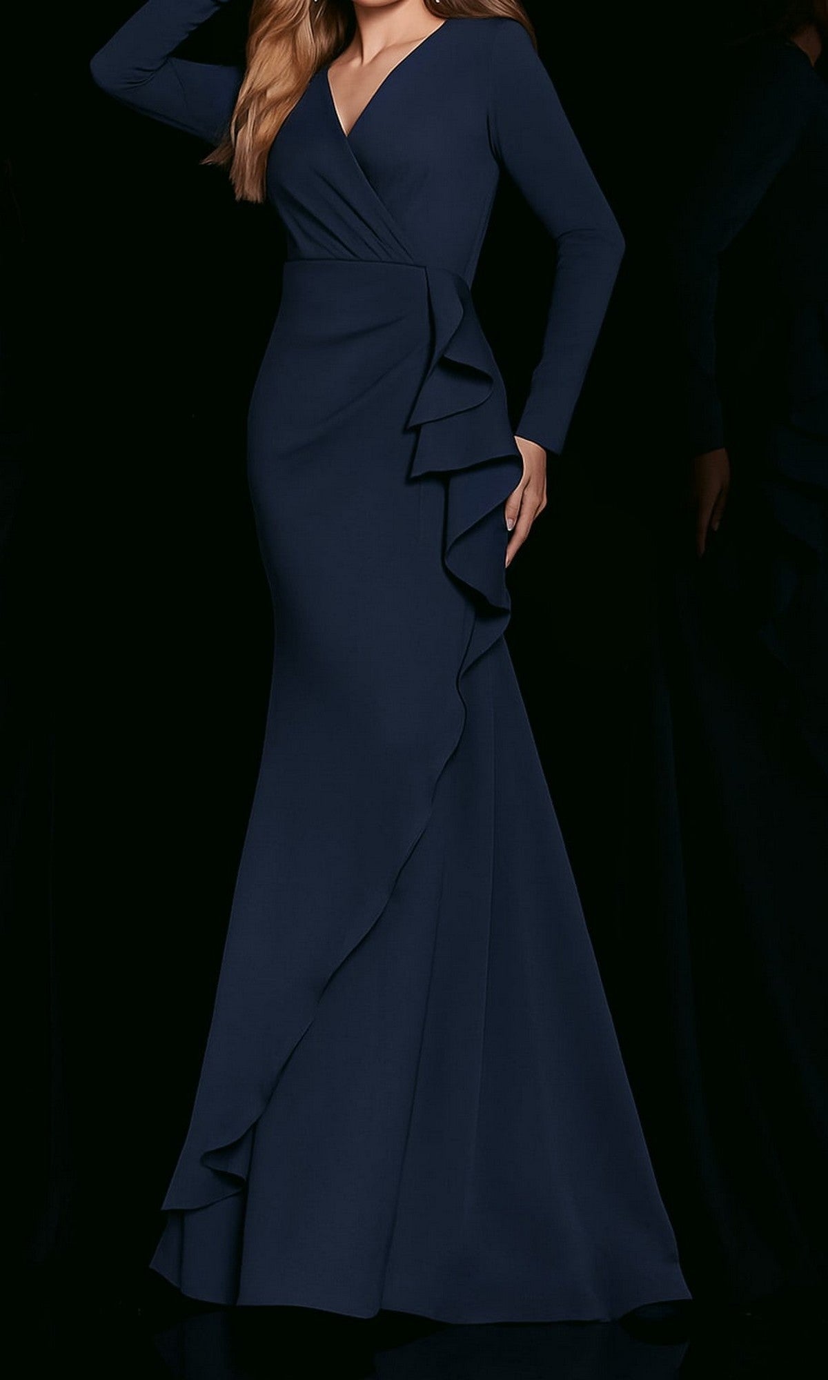 A woman showcases the Long-Sleeve Formal Designer Dress: Jovani 06995 in navy, featuring a floor-length silhouette with a v-neckline, wrap-style bodice, and ruffled detailing along the skirt, set against a black background.