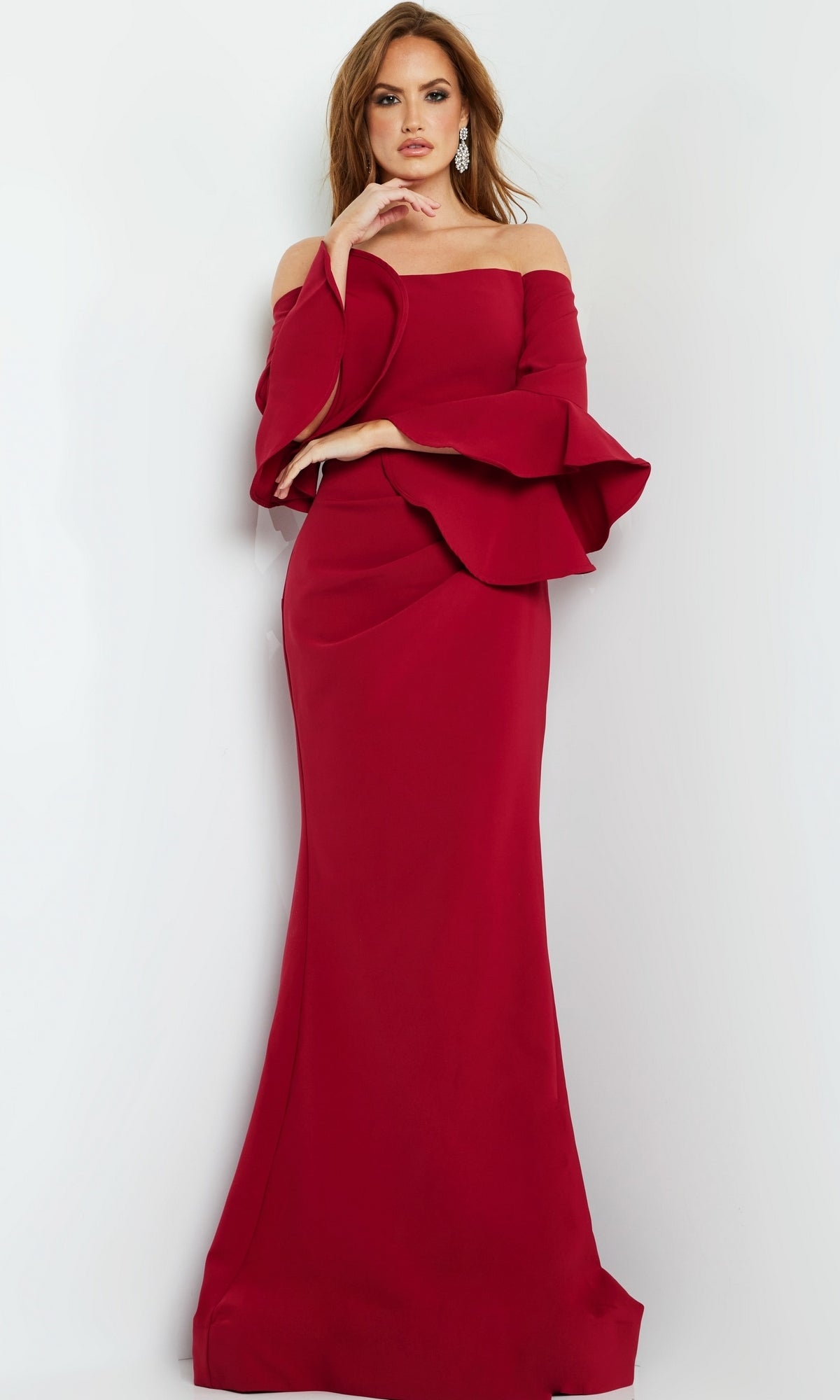 A woman poses against a white background wearing the Jovani 07065 Bell-Sleeve Designer Evening Gown, an elegant, off-the-shoulder red dress with flared sleeves and a fitted silhouette.