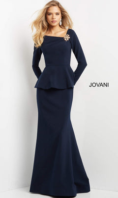 A woman wearing the Jovani 07131 long formal dress—a navy blue, long-sleeved peplum evening gown with a trumpet silhouette and a jeweled brooch at the shoulder—stands against a white background with “JOVANI” printed on the wall.