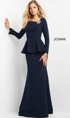 A woman stands against a white background with the word “JOVANI” beside her, wearing the Long Formal Dress: Jovani 07131, a long-sleeved navy gown accented with a peplum and a decorative shoulder brooch.