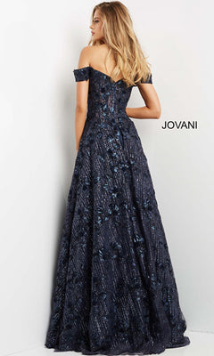 A woman wearing the Long Prom Dress 07162 by Jovani—navy blue, off-the-shoulder, with a floral pattern—stands facing a white wall displaying the word "JOVANI.