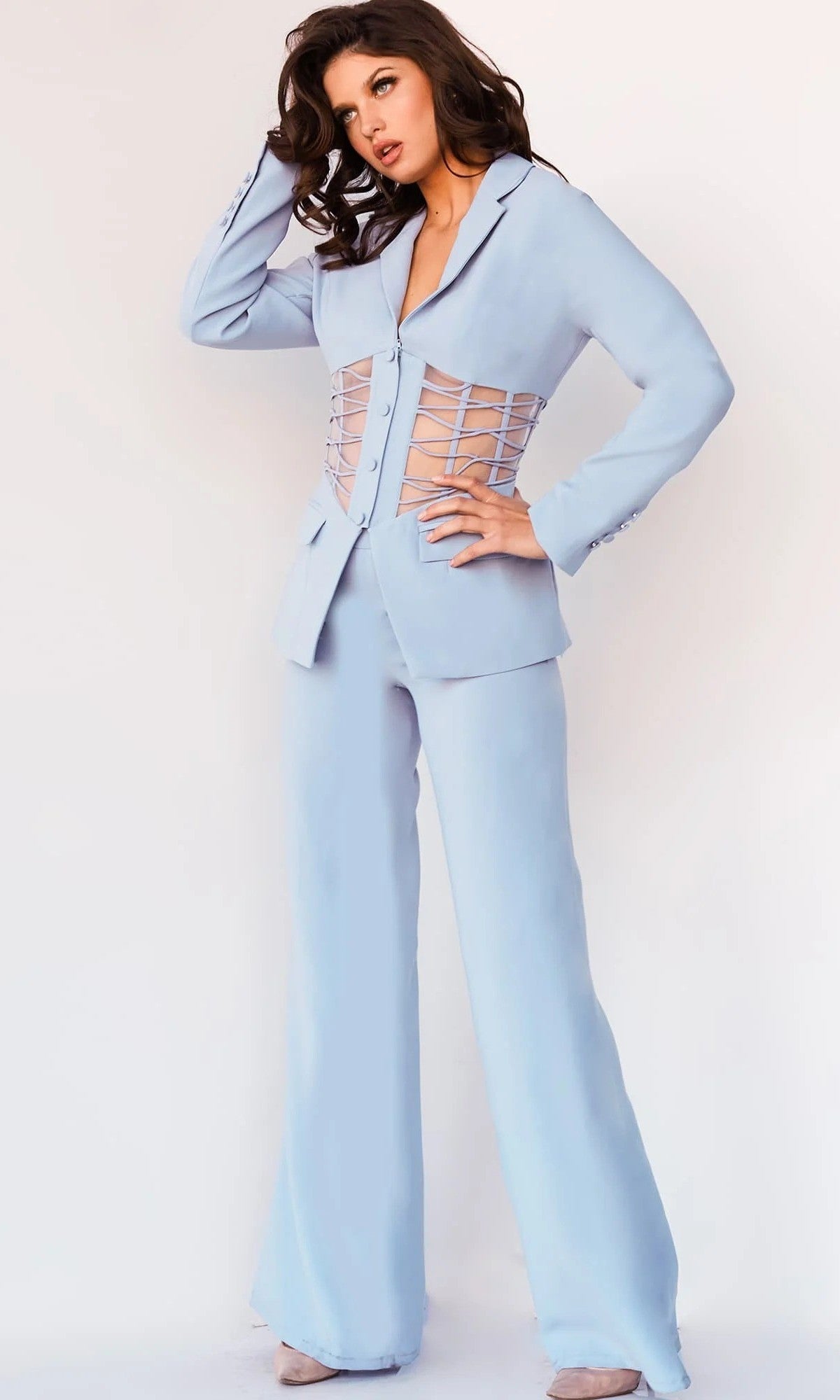 A woman wears the Jovani 07227 Long Jumpsuit in light-blue, featuring lace-up details on the sides of the blazer—a chic take on classic tailoring that captures the confidence of modern pantsuit style.