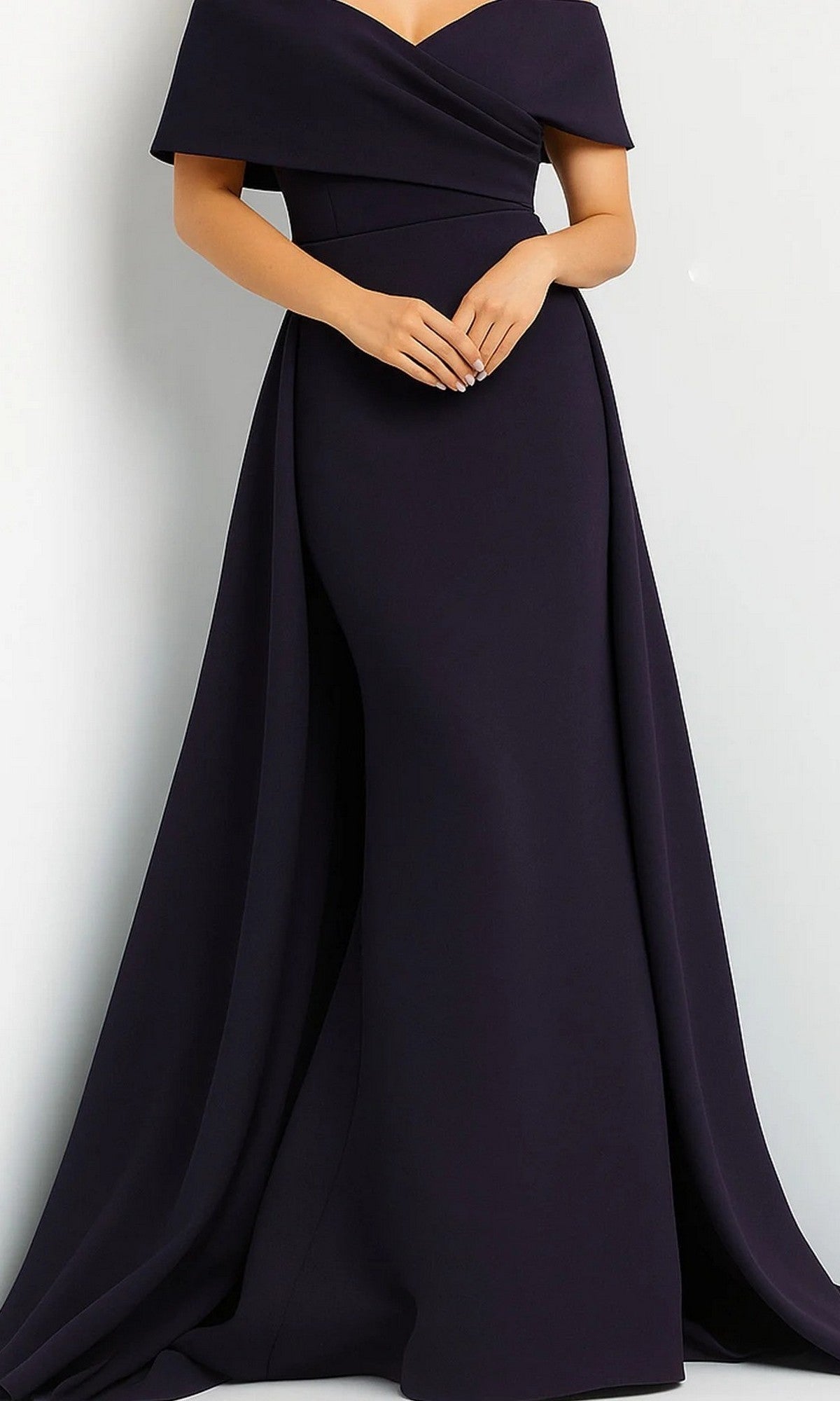 A person wearing the Jovani 07443 Long Formal Dress in navy, featuring an off-the-shoulder neckline, draped fabric, and a subtle mermaid skirt, stands against a plain light background.
