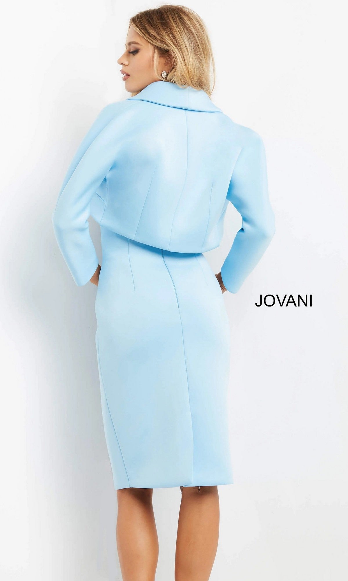 A woman is shown from the back, wearing the Jovani 07556 short wedding guest dress—a light blue, tailored, knee-length design with long sleeves and a collar—standing against a plain white background with “JOVANI” displayed on the right.