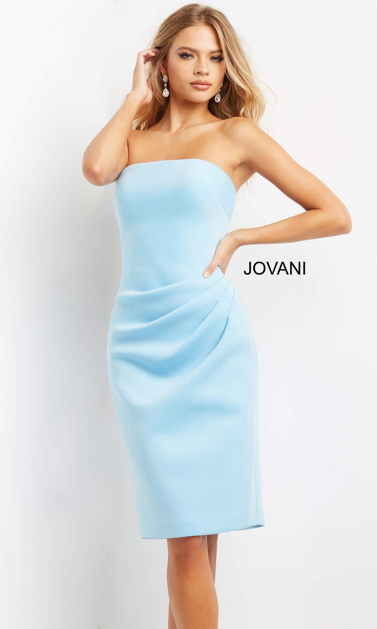 A woman stands against a white background wearing the Jovani 07556, a short wedding guest dress featuring a classic strapless bodice, light blue fitted silhouette, and subtle draping at the waist. The word “JOVANI” appears beside her.