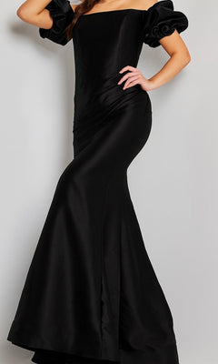 A woman models the Jovani 08361 Puff-Sleeve Mikado Evening Dress in black—a formal, floor-length gown featuring off-the-shoulder puffed sleeves and a subtle mermaid silhouette—as she poses with one hand on her hip against a plain background.