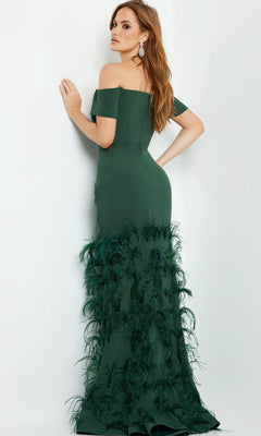 A woman models the Jovani 08384 Off-Shoulder Feather Mermaid Gown in dark green, featuring feather embellishments, as she poses stylishly over her shoulder against a plain white background.
