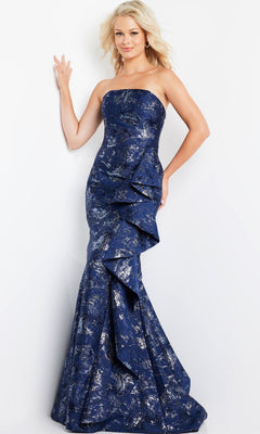 A woman stands against a plain white background wearing the Long Formal Dress: Jovani 08685—a strapless navy formal gown with a dark blue metallic finish, featuring an elegant ruffled detail and textured floral pattern reminiscent of glitter brocade.
