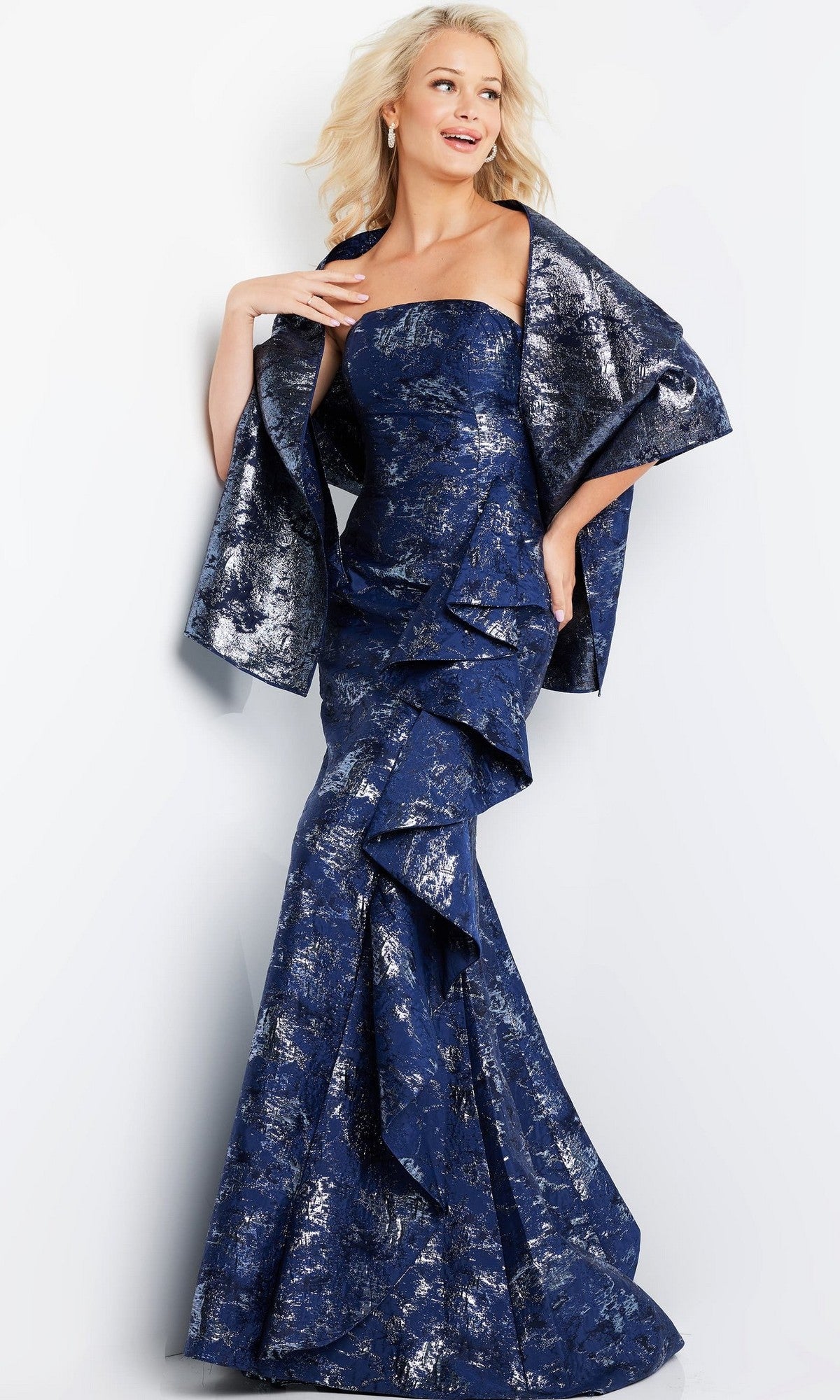 A woman stands against a plain light background, dressed in the Jovani 08685 long formal gown in navy—a strapless evening dress featuring shimmering metallic brocade patterns and complemented by a matching shawl, for an elegant and timelessly sophisticated look.