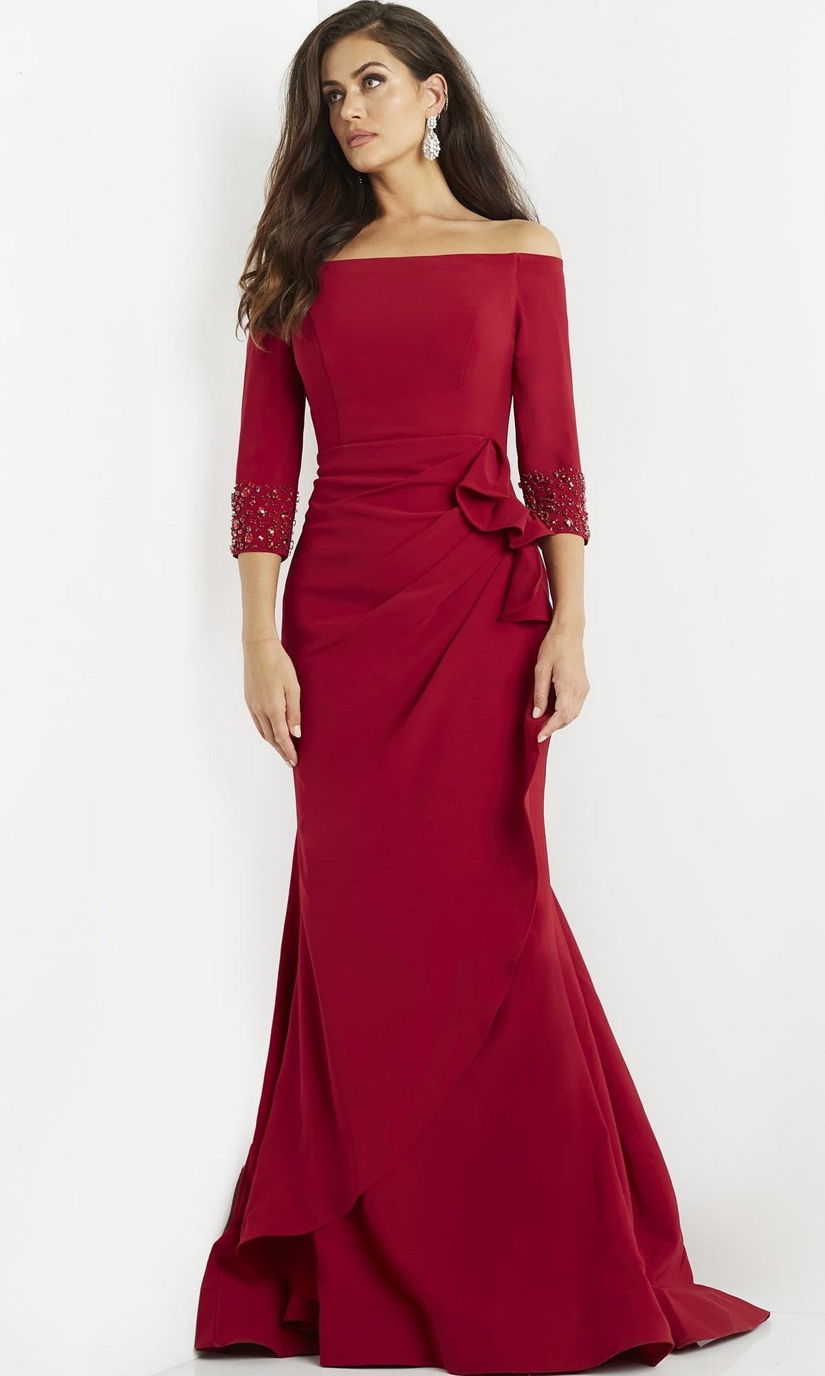 A woman wearing the Jovani 08699 Long Formal Dress, which features an off-the-shoulder design, three-quarter sleeves, and decorative details, stands against a plain white background.