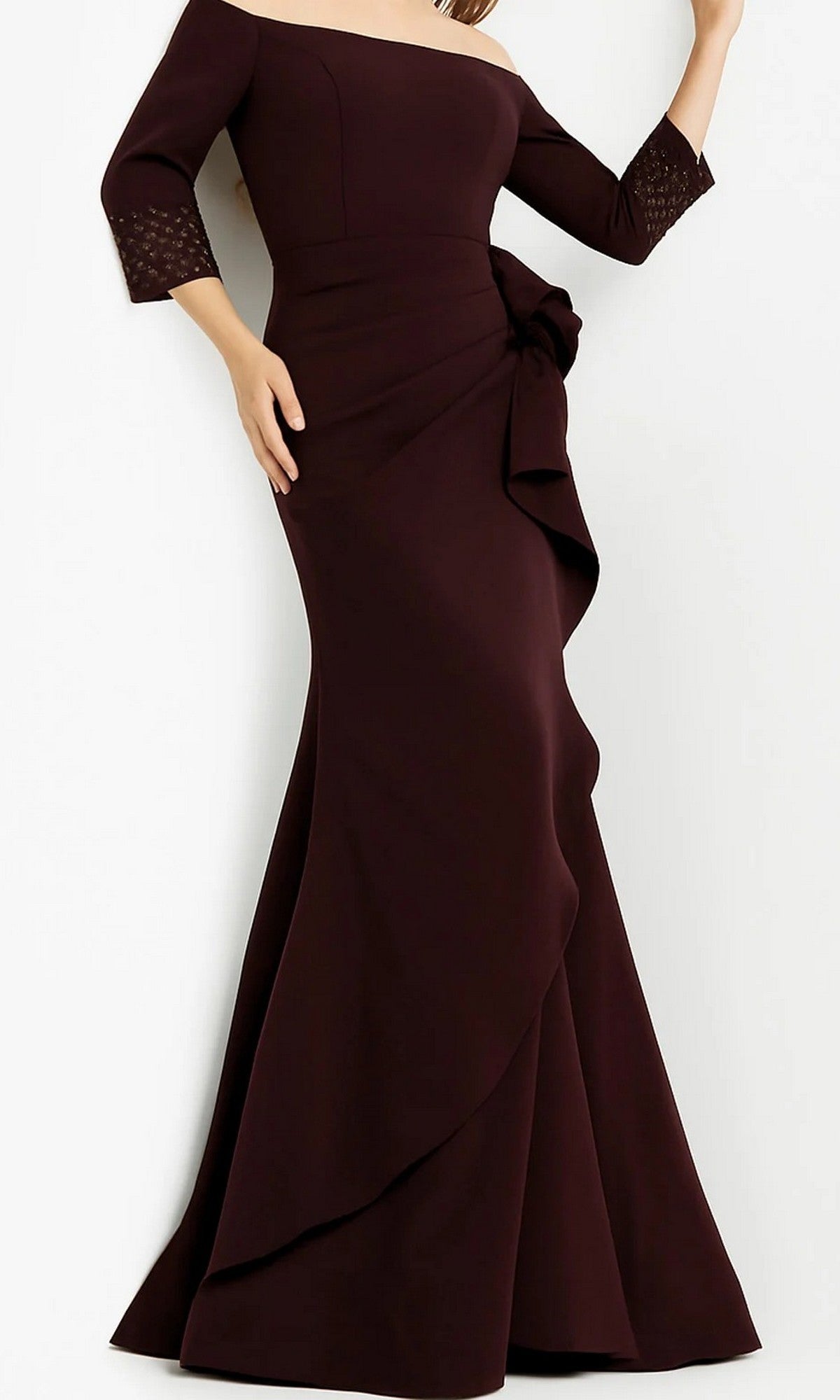 A woman wearing the Jovani 08699 long formal dress in plum, featuring an elegant off-shoulder design, three-quarter sleeves, a floor-length silhouette, and a large side bow detail.