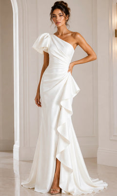 A woman wearing the Jovani 09201 long formal dress in white, featuring a one-shoulder design with ruffled detail, stands indoors against a light-colored wall and poses with one hand on her hip.