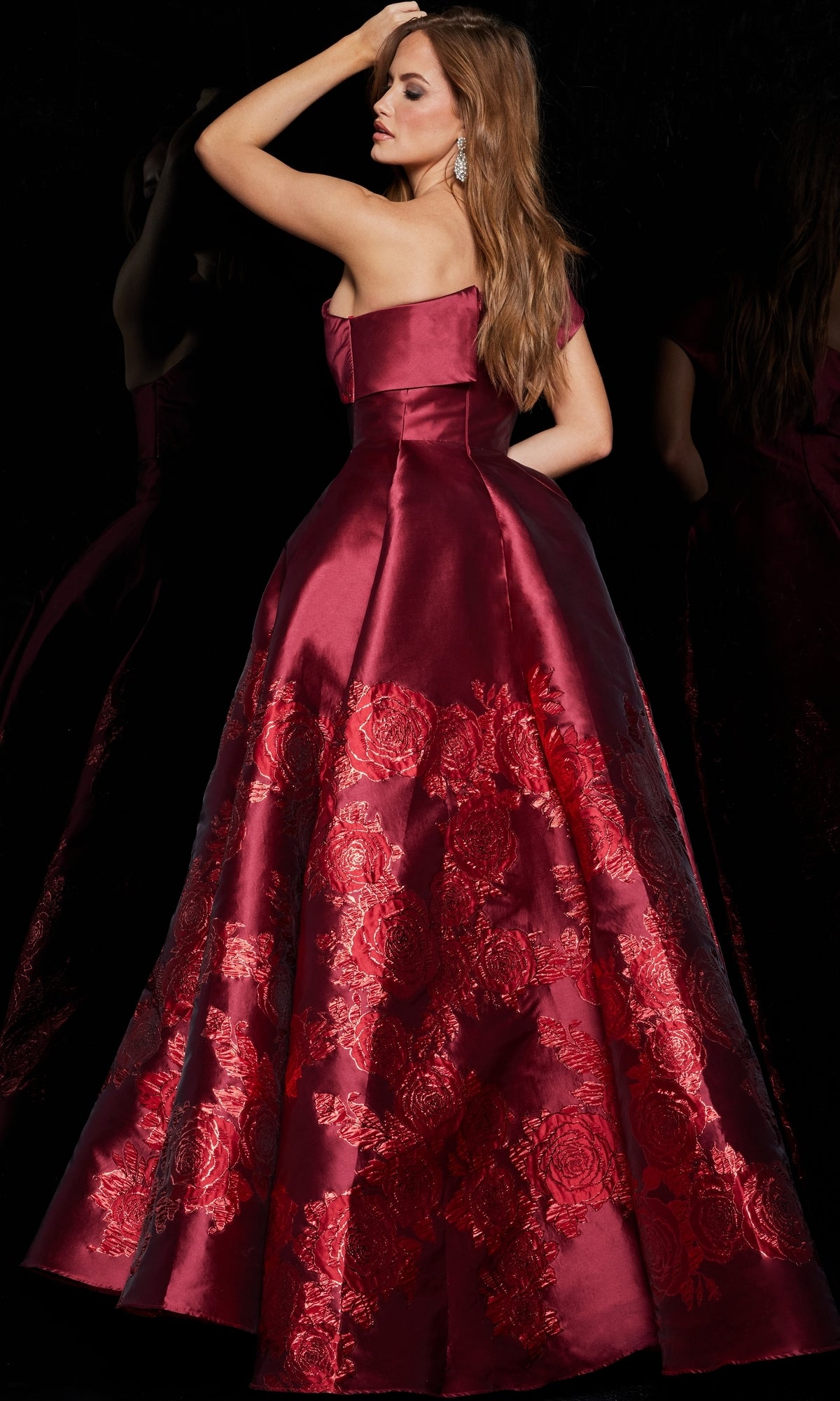 A woman poses against a black background, looking over her shoulder in the Jovani Long Red One-Shoulder Prom Ball Gown 09610 with floral embroidery.