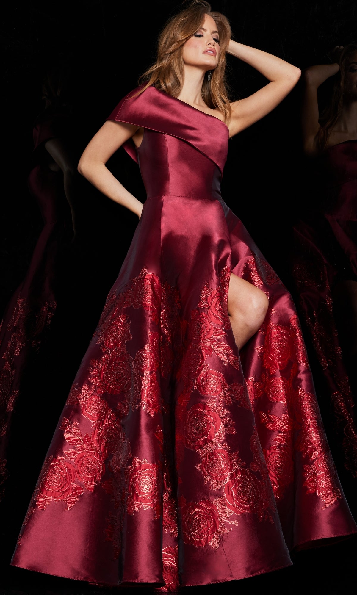 A woman poses in the Jovani Long Red One-Shoulder Prom Ball Gown 09610, featuring deep red satin, an asymmetrical neckline, floral embroidery, a high slit, and a full skirt.