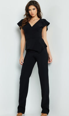 A woman stands against a light background wearing the Jovani 09646 Black Formal Jumpsuit, featuring a v-neck, short flared sleeves, and wide-leg pants, paired with brown shoes.