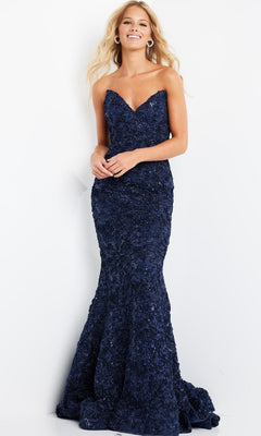 A woman stands smiling against a plain white background, wearing the Jovani 09768 long formal dress—a strapless, navy blue, floor-length gown featuring a textured floral pattern and an elegant mermaid silhouette.