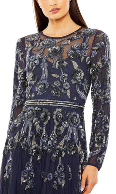 A woman wears the Mac Duggal 10013 long sleeve long blue formal dress, featuring sheer sleeves and intricate silver floral beadwork on the bodice, waist, and sleeves.