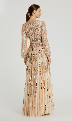 A woman stands facing away, wearing the Mac Duggal 10059 Long Beaded Bisque Formal Dress with long sleeves and floor-length sequined embellishments, her hair tied back in a low ponytail.