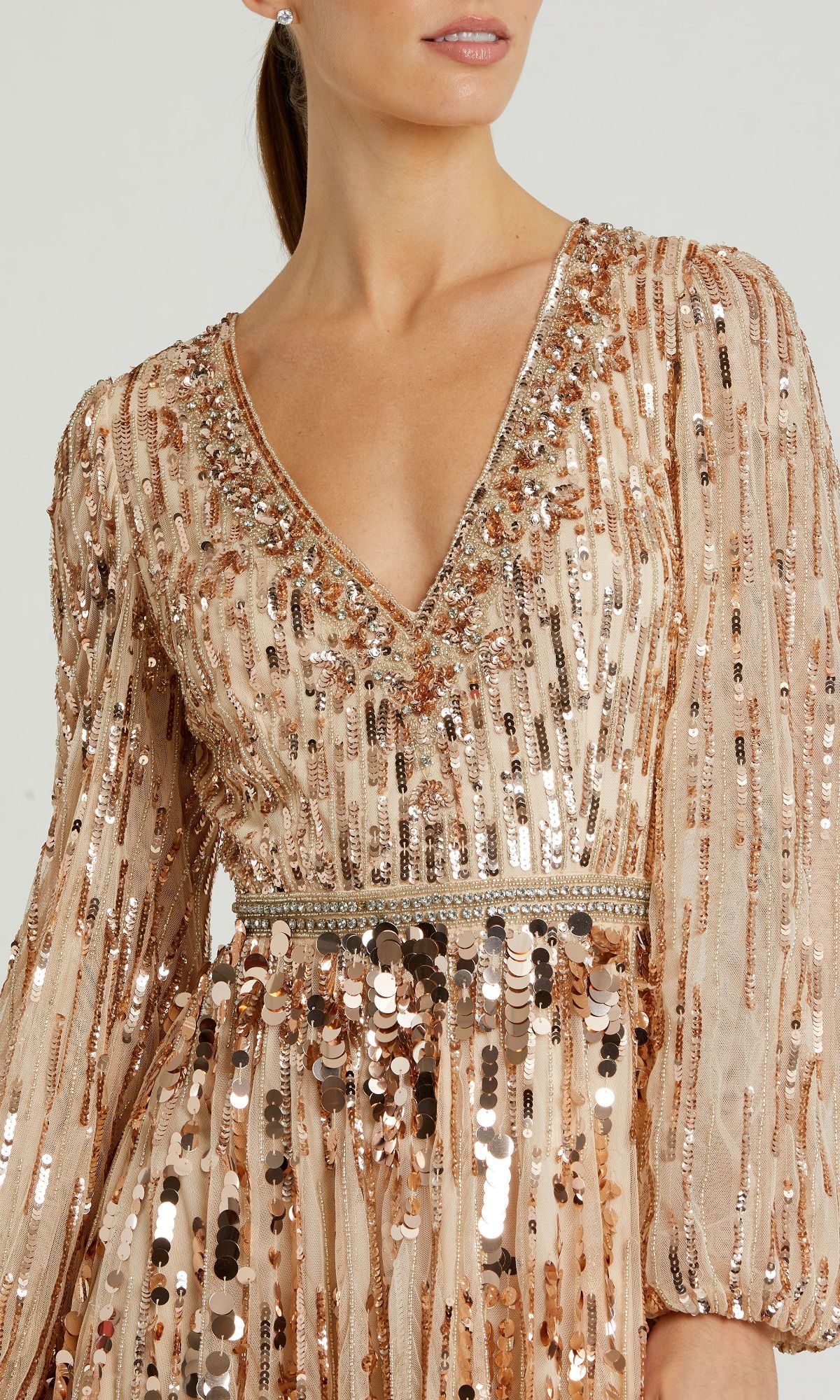 A woman wearing the Mac Duggal 10059 Long Beaded Bisque Formal Dress, featuring long sleeves, a V-neck, and sparkling gold and silver sequins with intricate beaded embellishments.