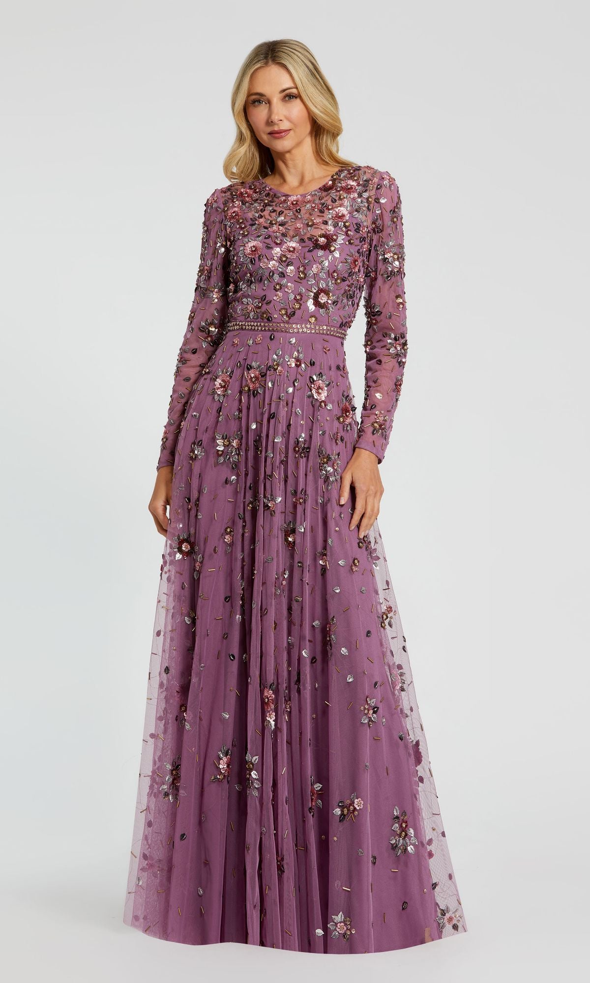 A woman wears the Mac Duggal 10063 Long Sleeve Beaded Formal Dress in lavender, adorned with floral embroidery and bead embellishments, standing against a plain background.