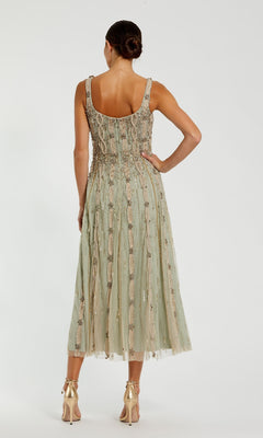 A woman faces away, wearing the Beaded Midi Wedding Guest Dress: Mac Duggal 10078 in sage green with a flared skirt, paired with gold high-heeled sandals.