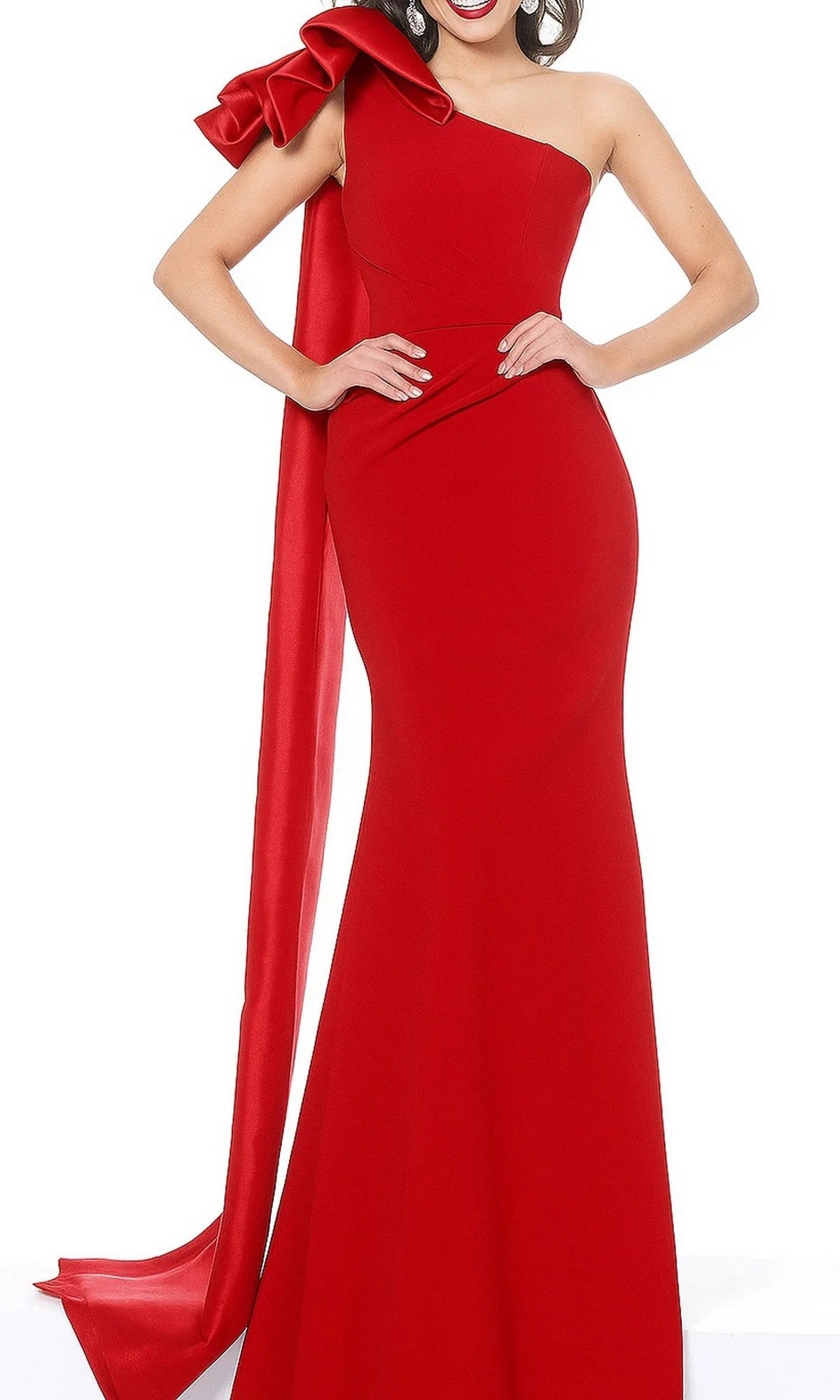 A woman wearing the Jovani 1008 Long Formal Dress in red—a fitted, floor-length, one-shoulder sheath gown featuring a large bow and an elegant long draping sash on the left shoulder.