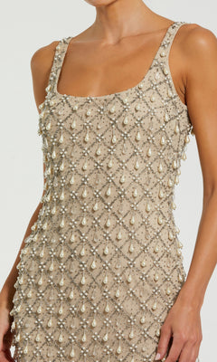 A person modeling the Mac Duggal 10084 Long Formal Dress—a sleeveless, tea-length beige dress adorned with crisscrossed lines of pearls and beads—is shown from shoulder to hip against a plain background.