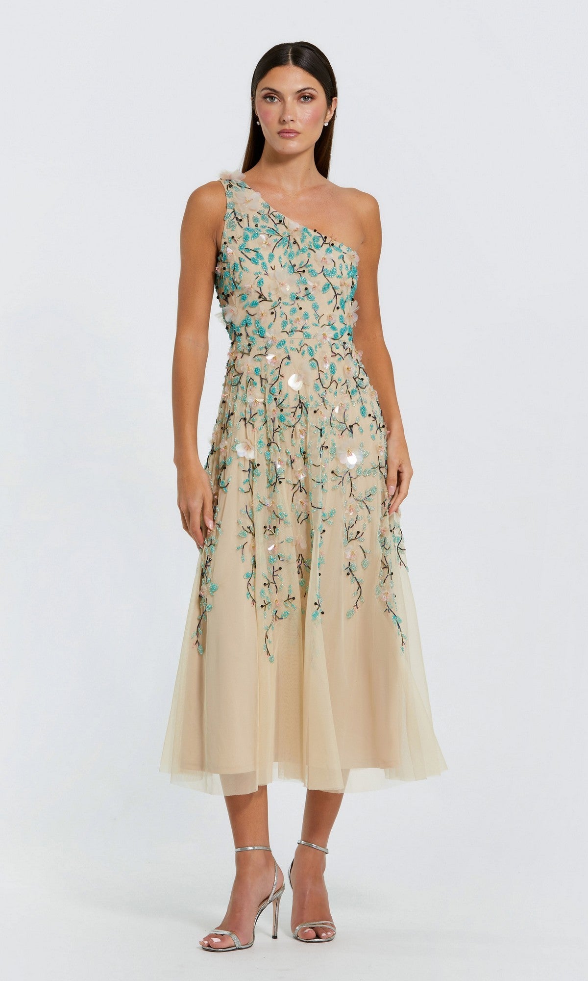 A woman in the Mac Duggal 10086 Midi Wedding Guest Dress in Nude Multi with floral embroidery and silver high heels stands against a plain light background, showcasing an elegant mid-length style perfect for special occasions.