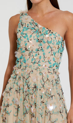 A woman in the Mac Duggal 10086 Midi Wedding Guest Dress, featuring a beige one-shoulder design with turquoise and white floral embroidery and sequin embellishments.