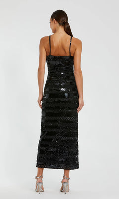 A woman stands with her back to the camera, wearing the Mac Duggal 10094 Midi Party Dress in black sequins with thin straps, paired with silver high-heeled sandals.