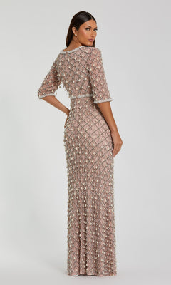 A woman stands facing away from the camera, wearing the Mac Duggal 10099 Beaded Long Pink Formal Dress—a fitted, floor-length gown in light mauve adorned with intricate beading and embellishments.