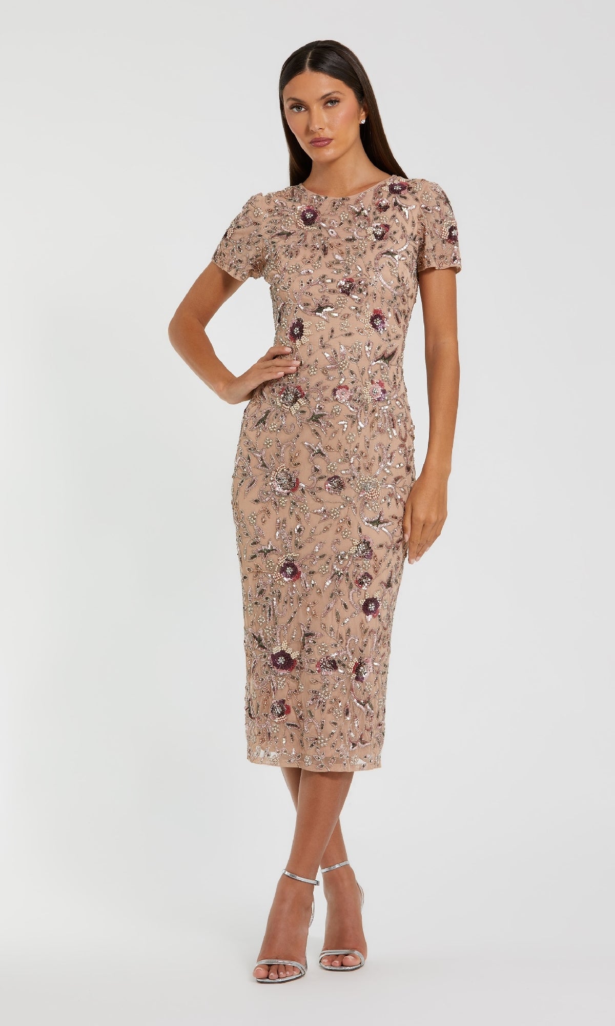 A woman models the Mac Duggal 10102 Beaded Midi Wedding Guest Dress, featuring a fitted beige silhouette with floral embroidery, posing against a plain background with one hand on her hip.