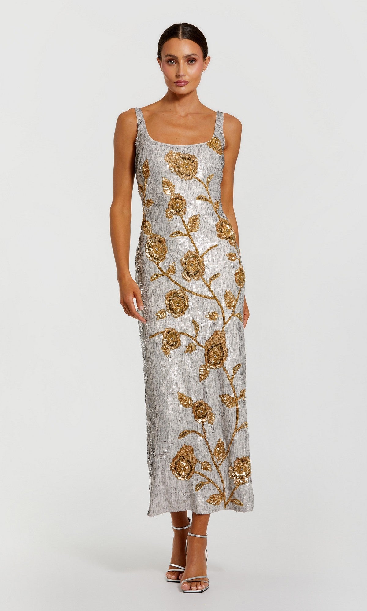 A woman wearing the Long Formal Dress: Mac Duggal 10119 in Platinum Gold—a sleeveless formal gown featuring gold floral sequin embroidery—stands against a plain light background.