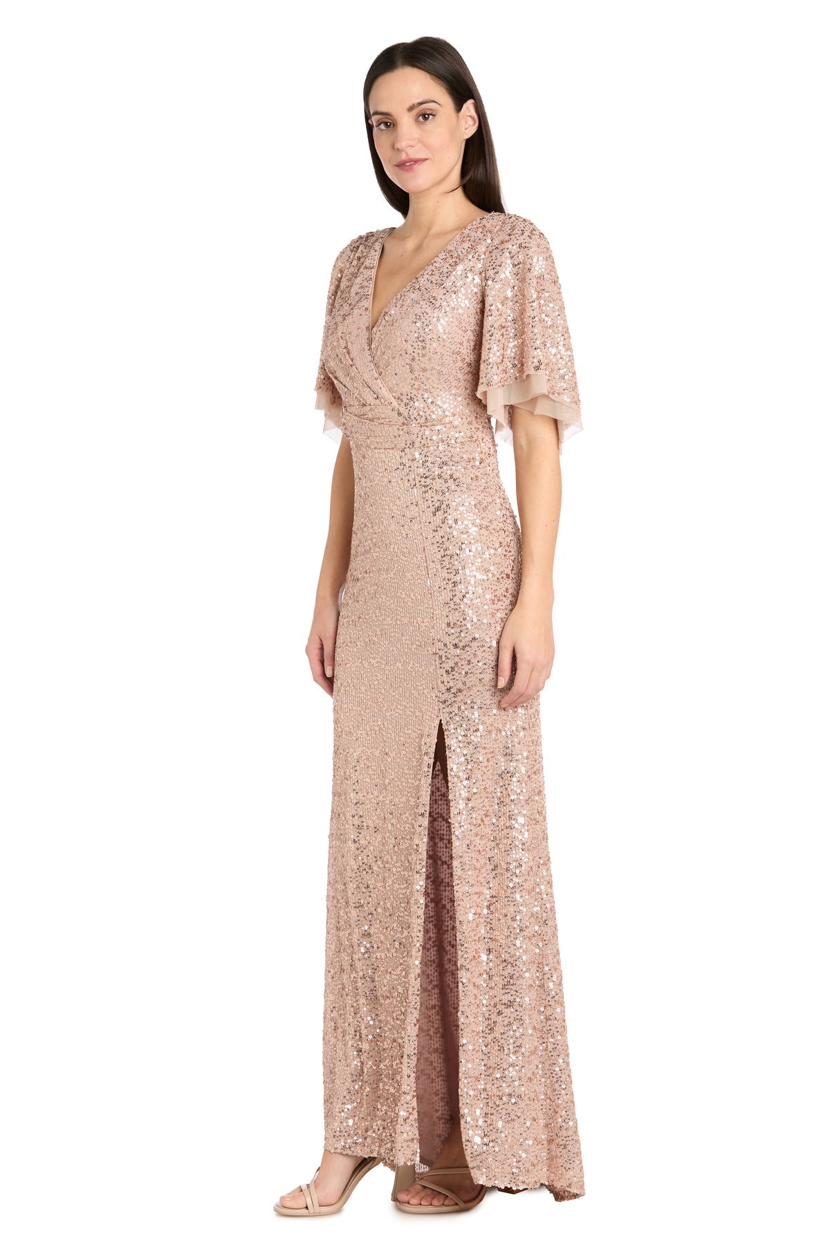 A woman wears the R&M Richards 1011 Rose Gold Sequin Formal Dress, featuring a floor-length silhouette, V-neckline, short flutter sleeves, and a side slit, set against a plain white background.