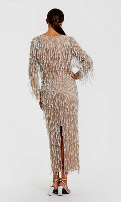 A woman with her hair in a low ponytail faces away, wearing the Midi Wedding Guest Dress: Mac Duggal 10120— a sheer nude midi dress with pearl beaded fringes—paired with metallic high-heeled sandals.