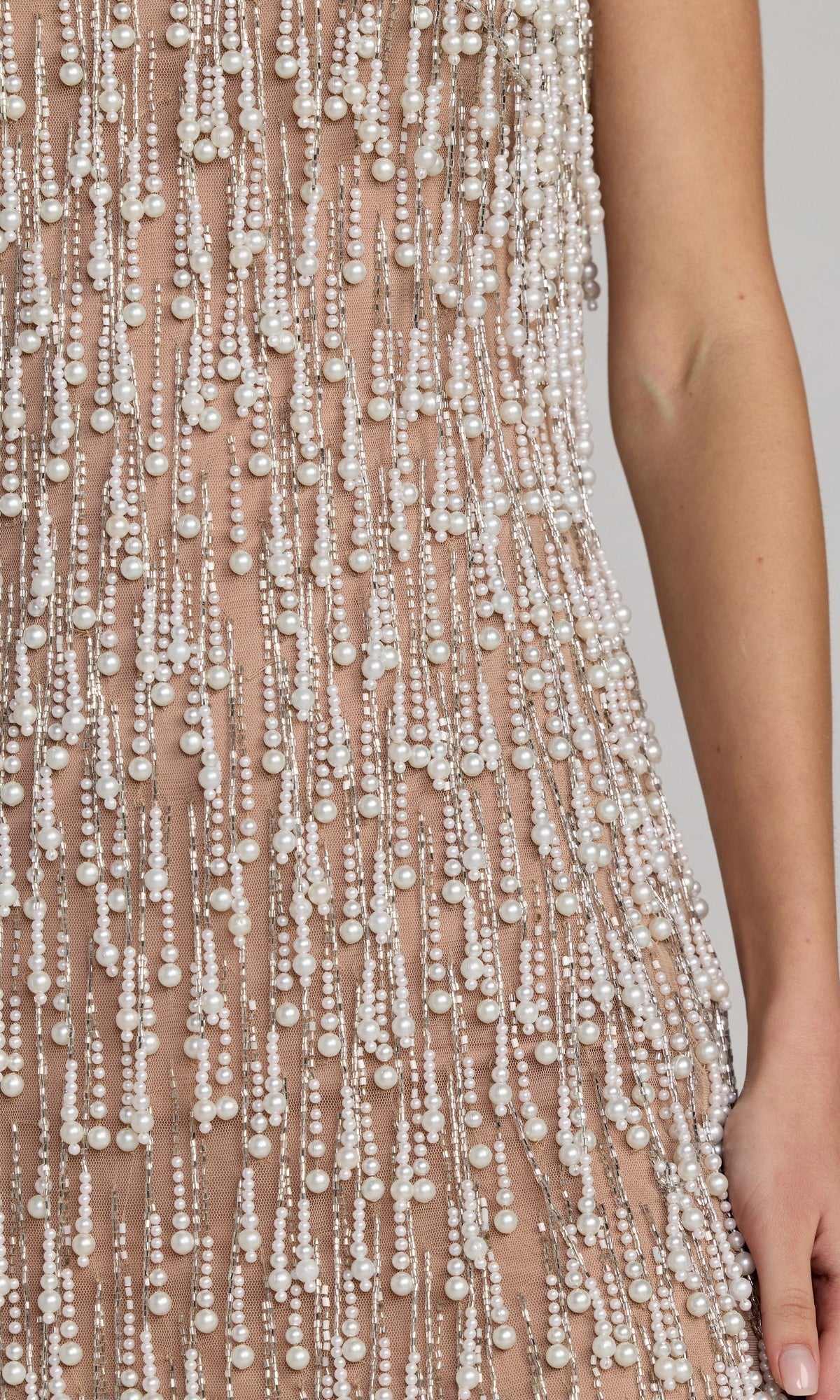 A close-up of the Short Cocktail Dress: Mac Duggal 10121, a sleeveless mini cocktail dress adorned with cascading strings of small white beads and pearl fringe, shown worn with a bare arm visible.