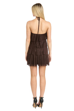 A woman is standing with her back to the camera, wearing the Morgan 10196 Short Homecoming Dress, which features a brown hue, a halter neckline, and elegant ruffled tiers, paired with black high-heeled shoes.