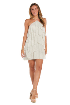 A woman stands and smiles, wearing the Short Homecoming Dress: Morgan 10196—a sleeveless, light-colored mini dress with a halter neckline and ruffled tiers—paired with beige high-heeled sandals.