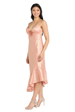 A woman in the Morgan 10251 Shimmer Midi Semi-Formal Dress—pink, shimmery, with spaghetti straps, rose chest detail, and ruffled hem—pairs it with silver heels for a chic party-ready look.