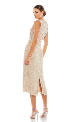 A woman stands against a white background wearing the Mac Duggal 10509 short sequin wedding guest dress—sleeveless, knee-length, beige, with a back slit—paired with silver high-heeled sandals.