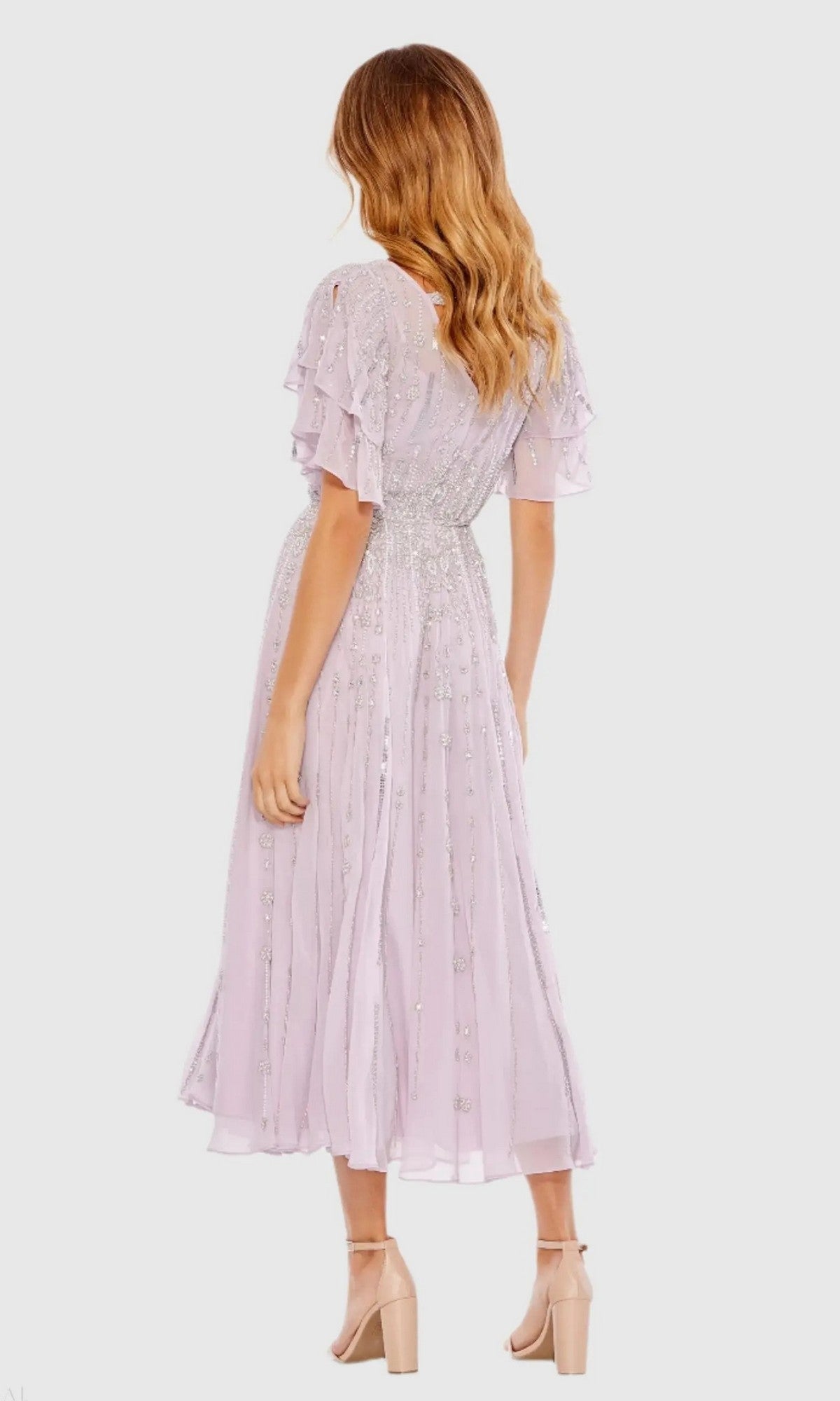 A woman faces away, wearing the Mac Duggal 10690 lilac sequin midi wedding guest dress with ruffled sleeves and nude block-heel sandals.