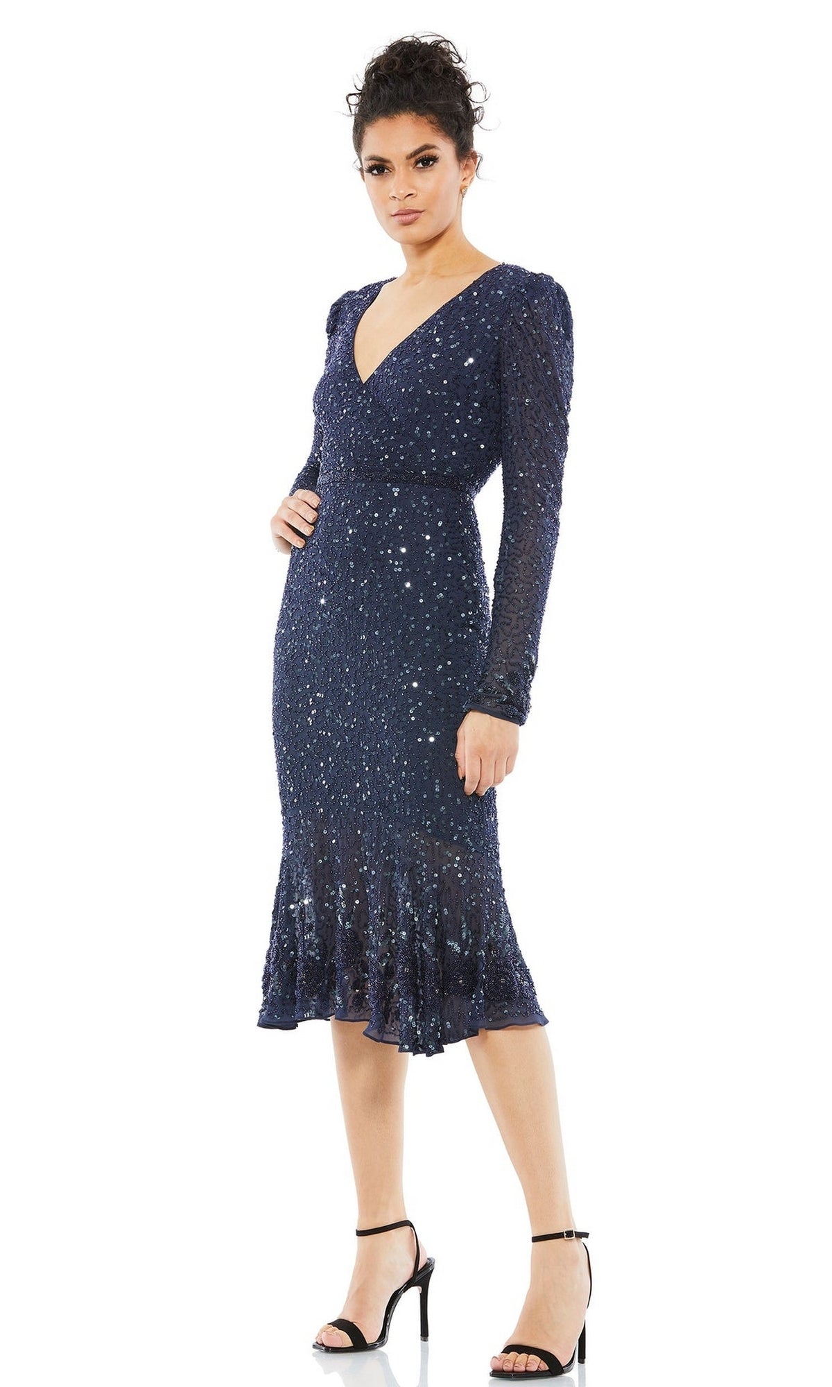 A person wears the Mac Duggal 10740 long sleeve wedding-guest dress—a dark blue, sequin midi gown with a V-neckline and flared hem—paired with black high-heeled sandals for an elegant look.