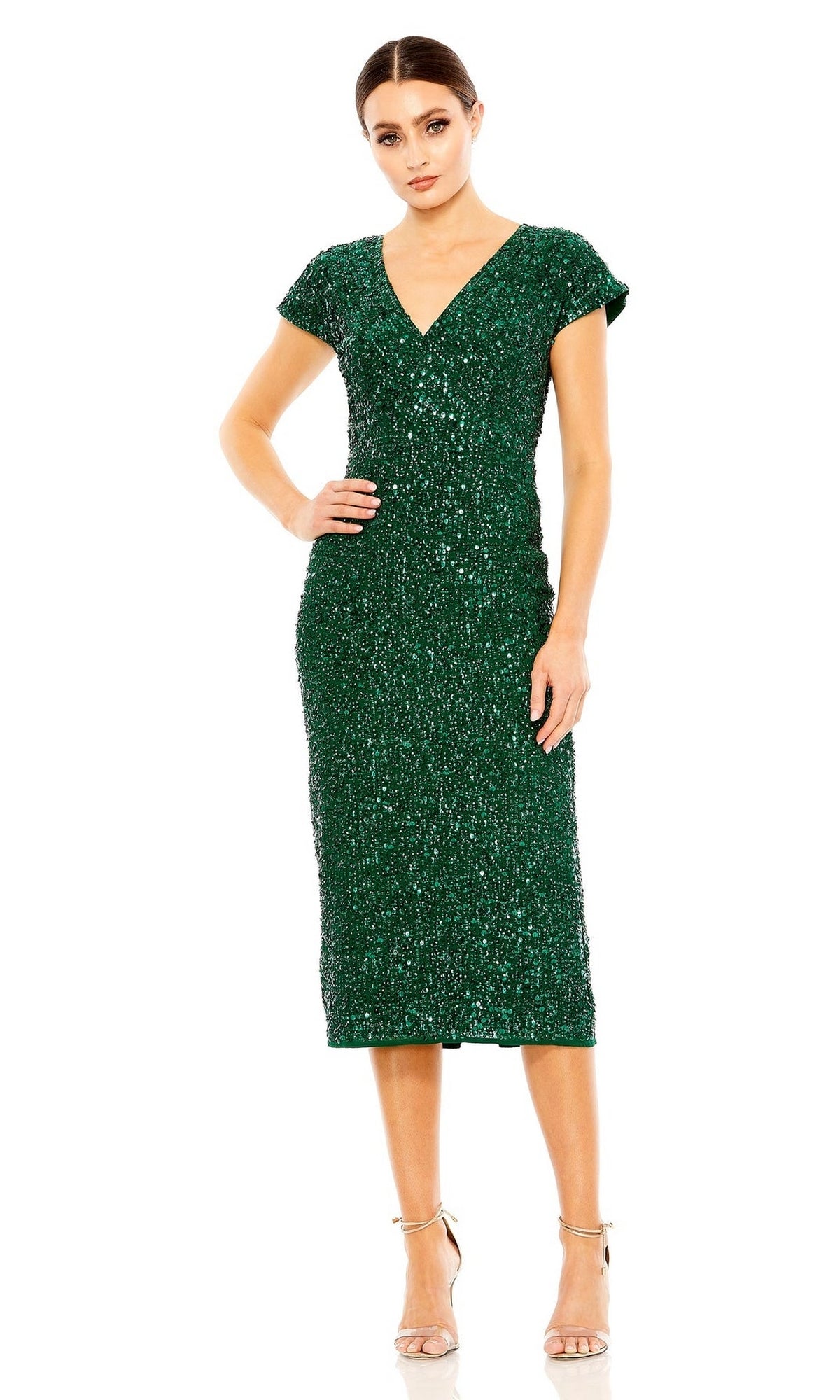 A woman stands in the Mac Duggal 10766 Midi Sequin Wedding Guest Dress with cap sleeves and shimmering sequins, paired with nude heels against a white background.