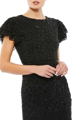 A woman poses with hands clasped in the Short Wedding Guest Dress 10771 by Mac Duggal—a fitted midi dress featuring textured floral accents and layered ruffle sleeves, perfect for an elegant semi-formal look.