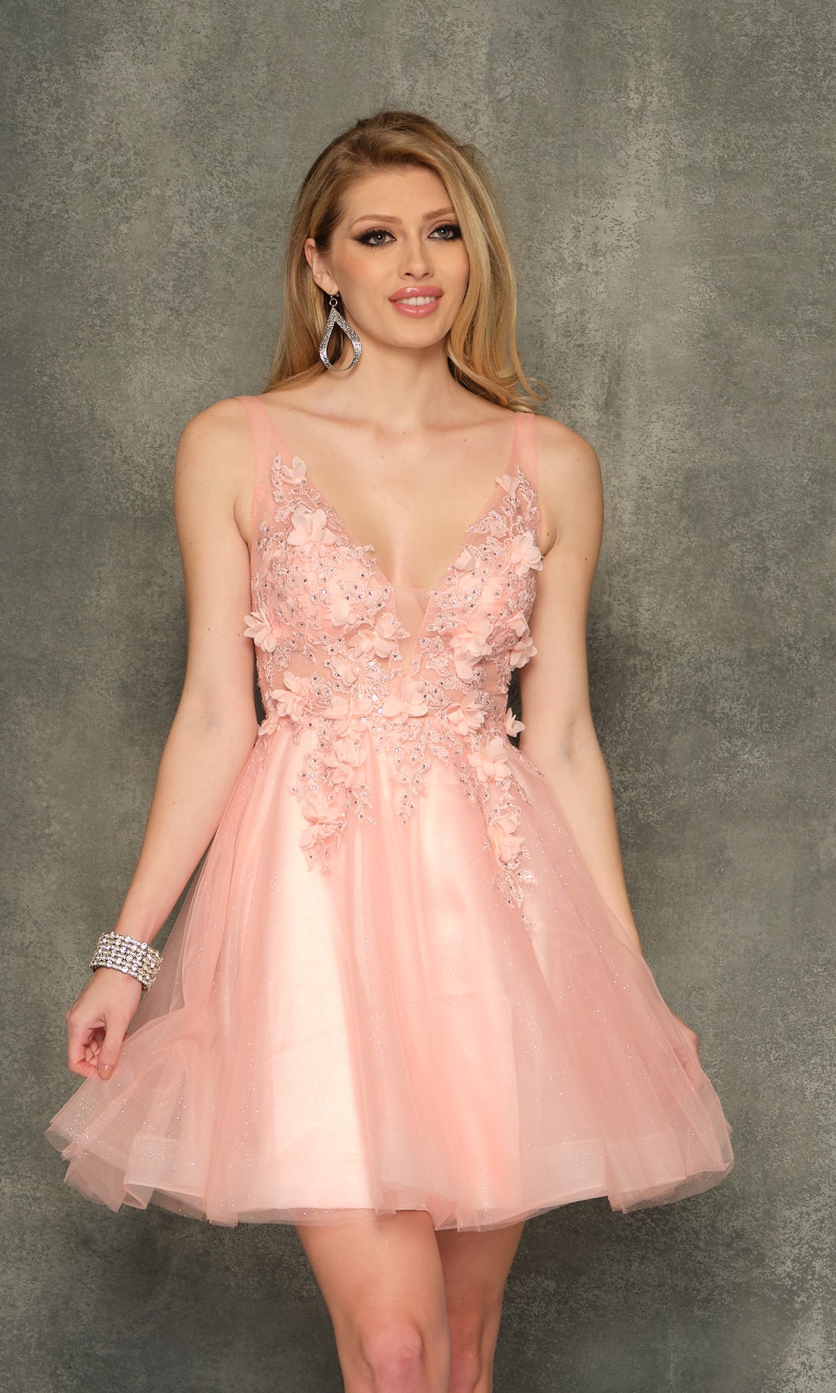 A woman in a sleeveless, light pink Sheer-Bodice Short Homecoming Dress stands before a textured gray background.