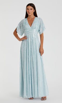 A woman models the Mac Duggal 10807, a short sleeve blue sequin formal dress with flutter sleeves and a deep V-neckline. The gown’s long A-line silhouette creates an elegant, modest evening look against a plain background.